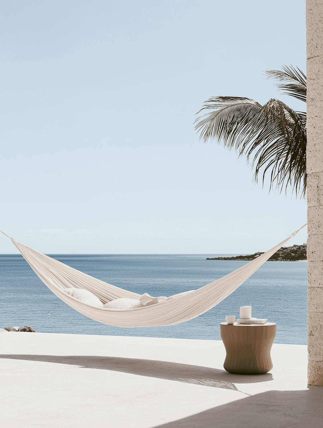 A hammock with cushions beside a small table holding a book and a cup